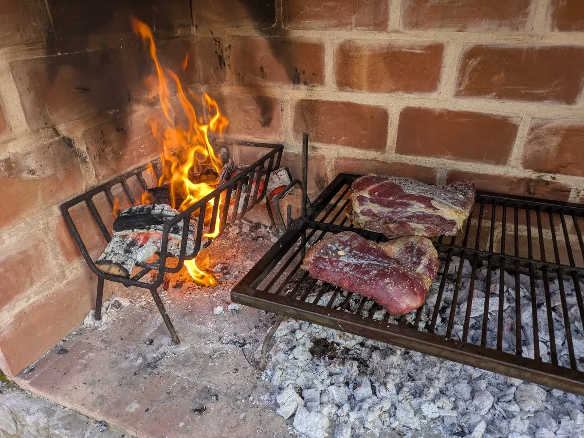 Meat grilling over wood embers on a brick parrilla
